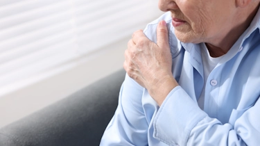 Чоловік торкається плеча через дискомфорт, що може бути пов’язаний зі скутістю, болем або порушенням руху після інсульту