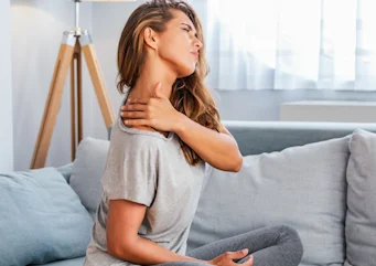 молода жінка торкається шиї через дискомфорт як ілюстрація до матеріалу про ознаки шийного остеохондрозу у клініці Медонія Прайм