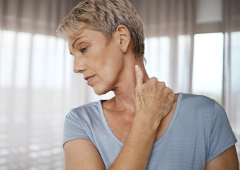 старша жінка відчуває дискомфорт у шиї як ілюстрація до матеріалу про відновлення при шийному остеохондрозі у клініці Медонія Прайм