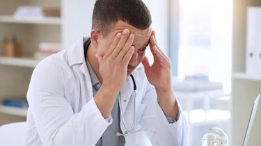 чоловік у білому халаті тримається за голову через сильний головний біль як ілюстрація до матеріалу про діагностику хронічного головного болю в клініці Медонія Прайм