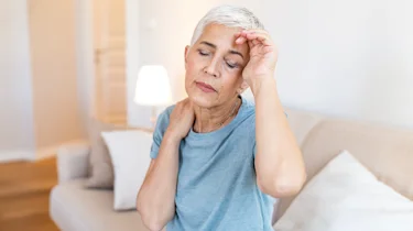 старша жінка тримається за голову через сильний біль у скронях як ілюстрація до матеріалу про консультацію при сильному головному болю в клініці Медонія Прайм