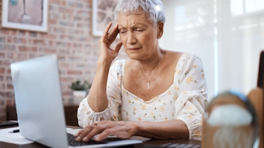 жінка сидить біля ноутбука і тримається за скроню через головний біль як ілюстрація до сторінки про лікування мігрені у клініці Медонія Прайм у Хмельницькому