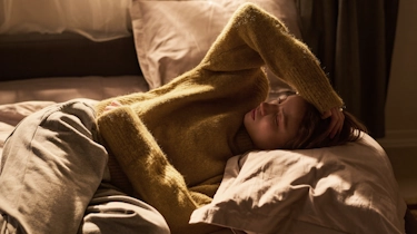 вагітна жінка лежить у ліжку та тримається за голову через головний біль як ілюстрація до матеріалу про причини головного болю під час вагітності у клініці Медонія Прайм