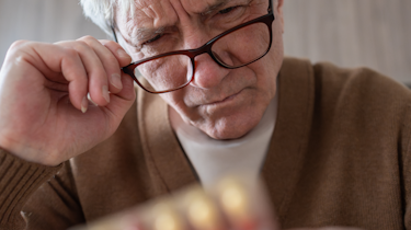 літній чоловік в окулярах дивиться на ліки як ілюстрація до матеріалу про препарати від головного болю у клініці Медонія Прайм