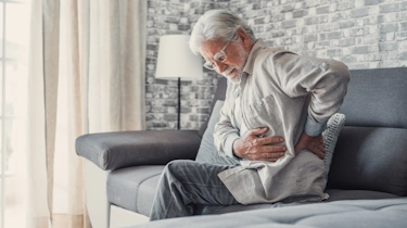 літній чоловік сидить і тримається за поперек через біль як ілюстрація до матеріалу про консультацію при болю в попереку у клініці Медонія Прайм