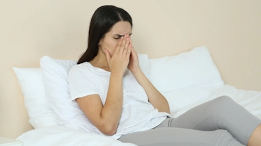 жінка сидить у ліжку та прикриває рот рукою через погане самопочуття як ілюстрація до матеріалу про головний біль з нудотою в клініці Медонія Прайм