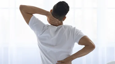 чоловік зі спини тримається за шию і поперек як ілюстрація до матеріалу про діагностику шийного остеохондрозу у клініці Медонія Прайм