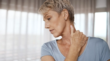 жінка старшого віку відчуває біль у шийному відділі як ілюстрація до матеріалу про допомогу при остеохондрозі у клініці Медонія Прайм