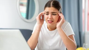 молода жінка тримається за скроні через головний біль як ілюстрація до матеріалу про обстеження при болю у скронях в клініці Медонія Прайм