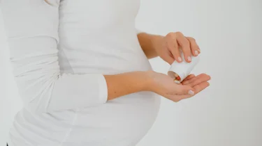 вагітна жінка тримає таблетку біля живота як ілюстрація до матеріалу про ліки від головного болю при вагітності у клініці Медонія Прайм