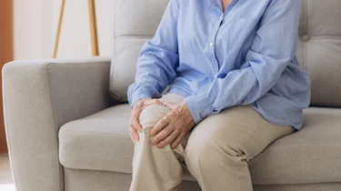 людина сидить і тримається за коліно як ілюстрація до матеріалу про рухові симптоми хвороби Паркінсона у клініці Медонія Прайм