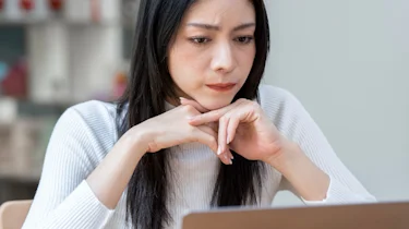 жінка сидить за ноутбуком і замислено тримає руки біля обличчя як ілюстрація до матеріалу про консультацію при частому головному болю в клініці Медонія Прайм