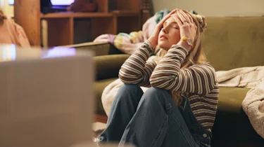 жінка на дивані тримається за голову через інтенсивний головний біль як ілюстрація до матеріалу про напад кластерного головного болю в клініці Медонія Прайм