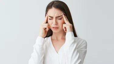 молода жінка тримається за скроні через запаморочення і нудоту як ілюстрація до матеріалу про обстеження у клініці Медонія Прайм