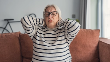 старша жінка в окулярах тримає руки за шиєю як ілюстрація до матеріалу про вправи для шиї при остеохондрозі у клініці Медонія Прайм