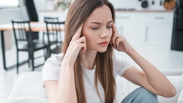 Жінка тримається за скроні через напруження, біль і дискомфорт у голові