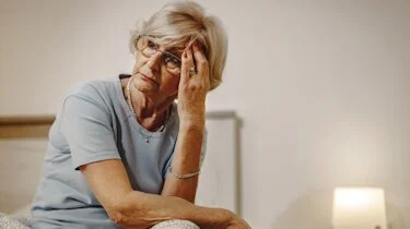 жінка похилого віку з болем у висках сидить удома як ілюстрація до матеріалу про лікування болю у висках в клініці Медонія Прайм