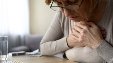 старша жінка сидить біля ліків і склянки води як ілюстрація до матеріалу про безпечний прийом ліків від головного болю у клініці Медонія Прайм