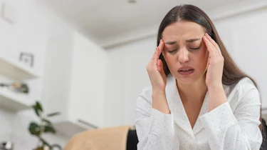 жінка тримається за скроні через симптоми кластерного головного болю як ілюстрація до матеріалу про лікування симптомів кластерного головного болю в клініці Медонія Прайм