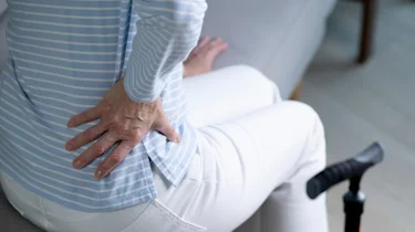 руки на попереку через біль у нижній частині спини як ілюстрація до матеріалу про фізичну реабілітацію при радикуліті попереку в клініці Медонія Прайм