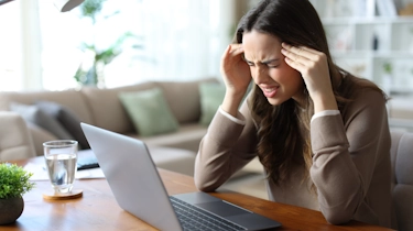 молода жінка за ноутбуком тримається за скроні через головний біль як ілюстрація до матеріалу про діагностику причин болю у скронях в клініці Медонія Прайм